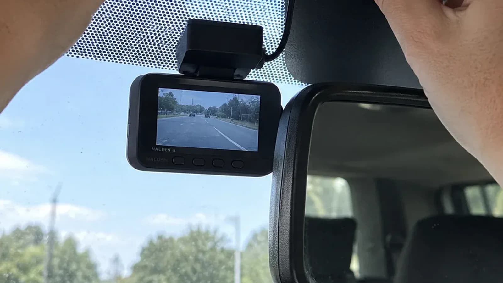 A small dash cam tucked behind a car's rear-view mirror with its cable hidden in the roof lining
