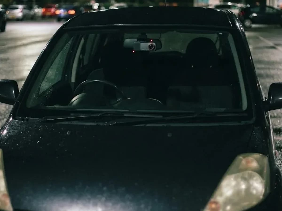 A hatchback parked in a supermarket car park at night with the small Halden camera behind its mirror