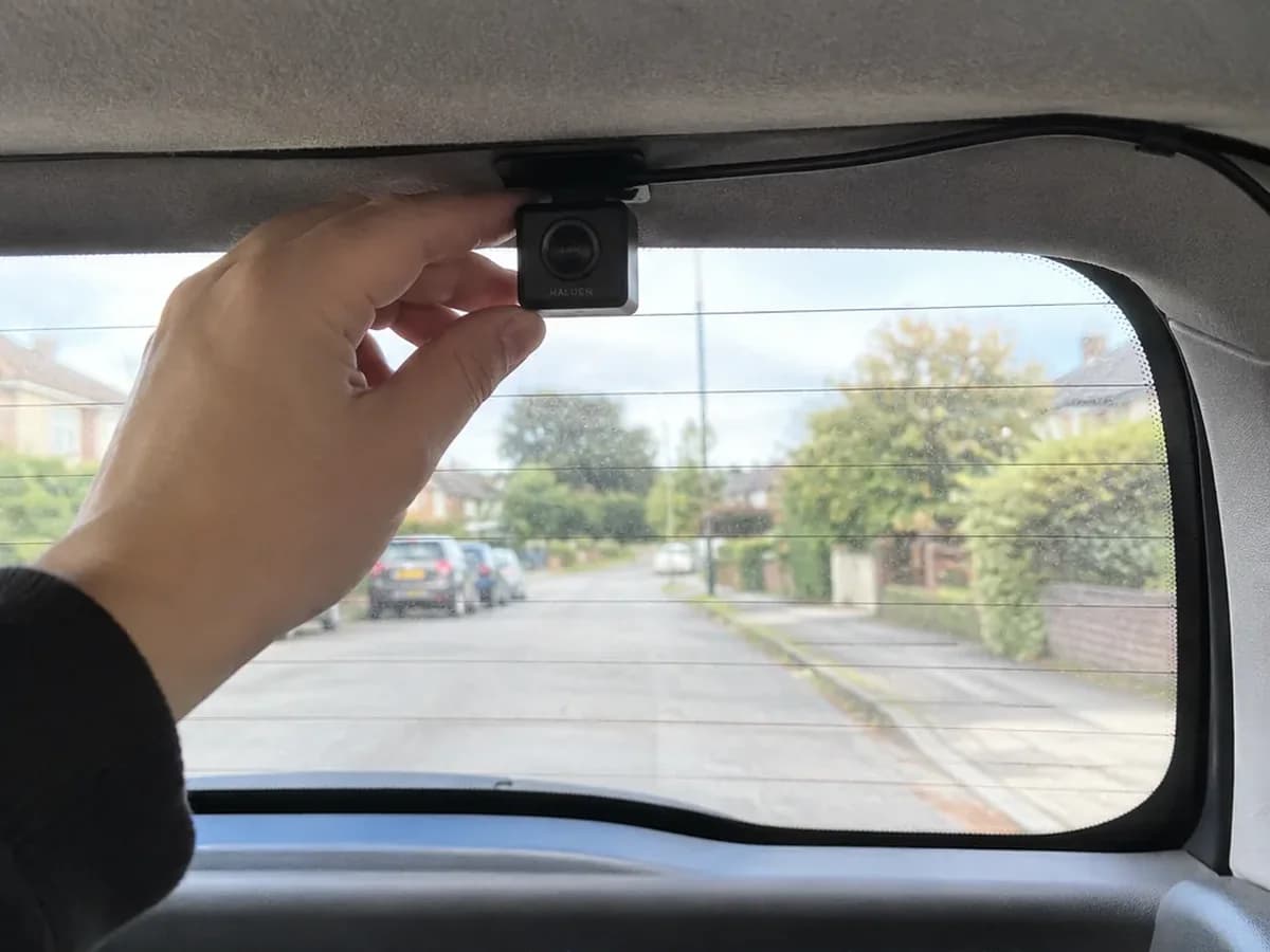 A hand sticking the small Halden rear camera inside the top of a hatchback's back window