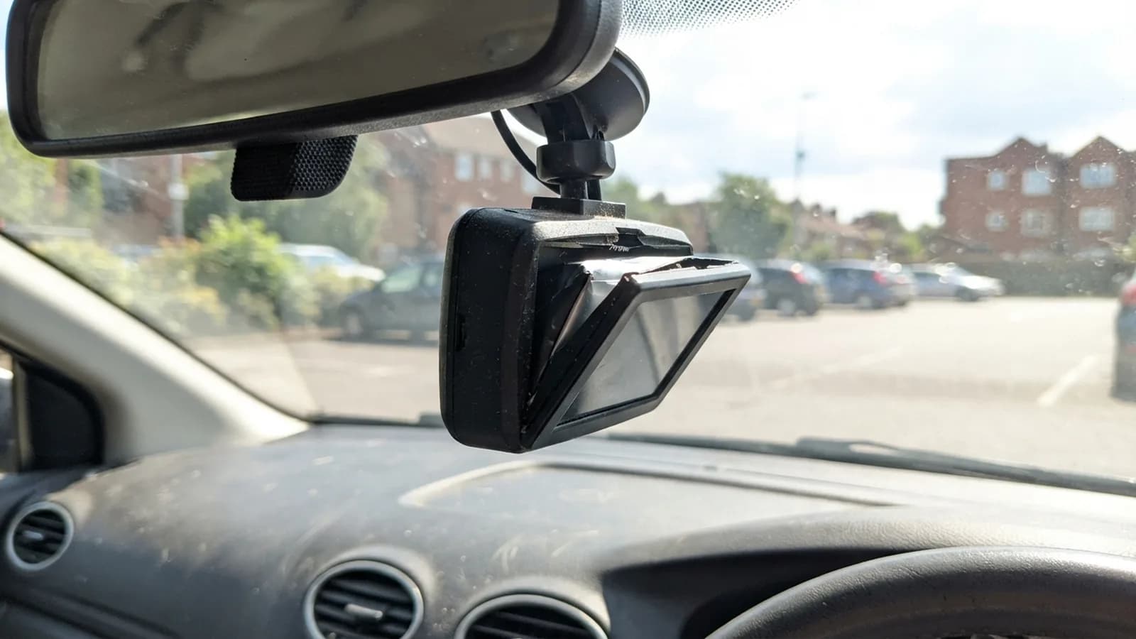 A cheap dash cam behind a car mirror on a sunny day with its screen pushed out of the case by a swollen battery